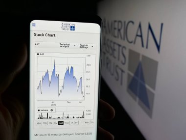 Stuttgart, Germany - 11-07-2025: Person holding cellphone with webpage of US REIT company American Assets Trust Inc. on screen in front of logo. Focus on center of phone display.