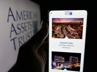 Stuttgart, Germany - 11-07-2025: Person holding smartphone with web page of US REIT company American Assets Trust Inc. on screen in front of logo. Focus on center of phone display.