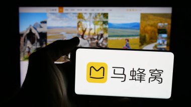 Stuttgart, Germany - 11-07-2025: Person holding mobile phone with logo of Chinese travel company Mafengwo.com on screen in front of web page. Focus on phone display.