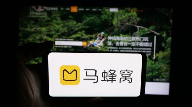 Stuttgart, Germany - 11-07-2025: Person holding cellphone with logo of Chinese travel company Mafengwo.com on screen in front of webpage. Focus on phone display.