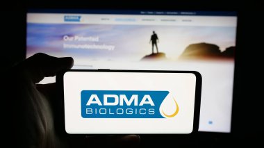 Stuttgart, Germany - 11-07-2025: Person holding cellphone with logo of US biopharma company ADMA Biologics Inc. on screen in front of webpage. Focus on phone display.