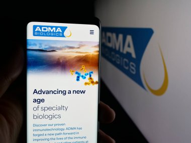 Stuttgart, Germany - 11-07-2025: Person holding cellphone with webpage of US biopharma company ADMA Biologics Inc. on screen in front of logo. Focus on center of phone display.