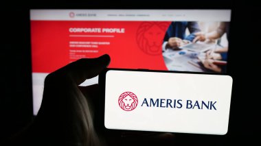 Stuttgart, Germany - 11-07-2025: Person holding mobile phone with logo of US financial services company Ameris Bank on screen in front of web page. Focus on phone display.