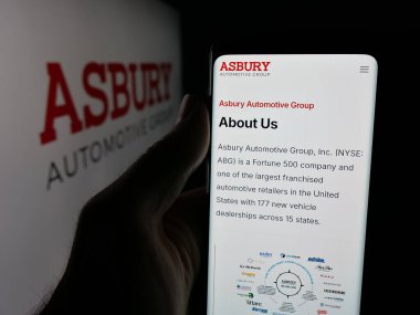 Stuttgart, Germany - 11-07-2025: Person holding smartphone with web page of US company Asbury Automotive Group Inc. on screen in front of logo. Focus on center of phone display.