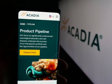 Stuttgart, Germany - 11-07-2025: Person holding smartphone with web page of biopharma company Acadia Pharmaceuticals Inc. on screen in front of logo. Focus on center of phone display.