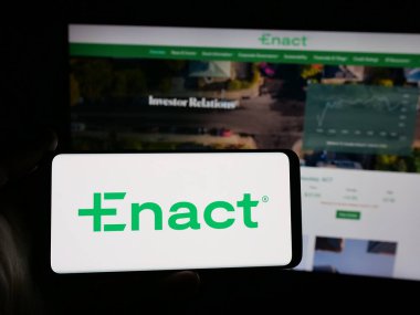 Stuttgart, Germany - 11-07-2025: Person holding smartphone with logo of US mortgage company Enact Holdings Inc. on screen in front of website. Focus on phone display.
