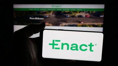 Stuttgart, Germany - 11-07-2025: Person holding mobile phone with logo of US mortgage company Enact Holdings Inc. on screen in front of web page. Focus on phone display.