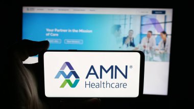 Stuttgart, Germany - 11-08-2025: Person holding cellphone with logo of staffing company AMN Healthcare Services Inc. on screen in front of webpage. Focus on phone display.