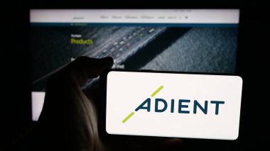 Stuttgart, Germany - 11-08-2025: Person holding mobile phone with logo of automotive seating company Adient plc on screen in front of web page. Focus on phone display.