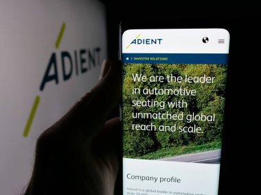 Stuttgart, Germany - 11-08-2025: Person holding cellphone with webpage of automotive seating company Adient plc on screen in front of logo. Focus on center of phone display.