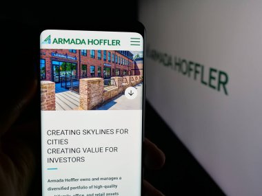 Stuttgart, Germany - 11-08-2025: Person holding cellphone with webpage of US company Armada Hoffler Properties Inc. on screen in front of logo. Focus on center of phone display.