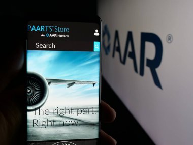 Stuttgart, Germany - 11-08-2025: Person holding cellphone with webpage of US aircraft maintenance company AAR Corp. on screen in front of logo. Focus on center of phone display.