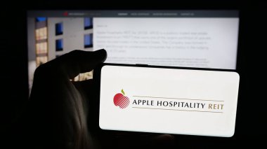 Stuttgart, Germany - 11-08-2025: Person holding mobile phone with logo of US company Apple Hospitality REIT Inc. on screen in front of web page. Focus on phone display.
