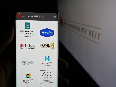 Stuttgart, Germany - 11-08-2025: Person holding smartphone with web page of US company Apple Hospitality REIT Inc. on screen in front of logo. Focus on center of phone display.