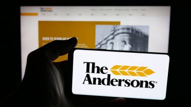 Stuttgart, Germany - 11-08-2025: Person holding mobile phone with logo of US agribusiness company The Andersons Inc. on screen in front of web page. Focus on phone display.