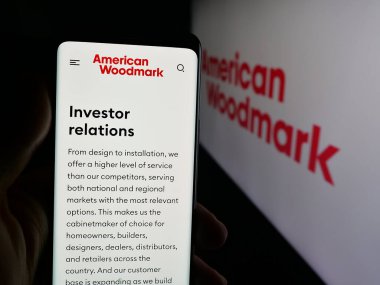 Stuttgart, Germany - 11-08-2025: Person holding cellphone with webpage of US company American Woodmark Corporation on screen in front of logo. Focus on center of phone display.