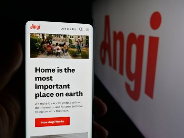 Stuttgart, Germany - 11-08-2025: Person holding cellphone with webpage of US online marketplace company Angi Inc. on screen in front of logo. Focus on center of phone display.
