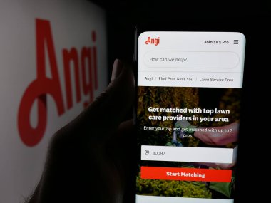 Stuttgart, Germany - 11-08-2025: Person holding smartphone with web page of US online marketplace company Angi Inc. on screen in front of logo. Focus on center of phone display.