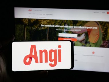 Stuttgart, Germany - 11-08-2025: Person holding smartphone with logo of US online marketplace company Angi Inc. on screen in front of website. Focus on phone display.