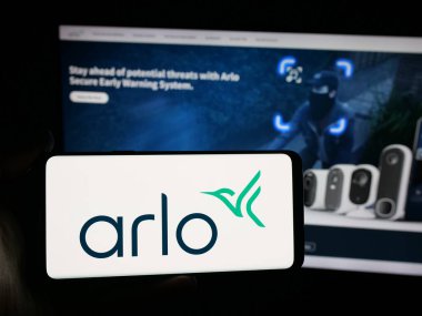 Stuttgart, Germany - 11-12-2025: Person holding smartphone with logo of US CCTV company Arlo Technologies Inc. on screen in front of website. Focus on phone display.
