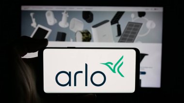 Stuttgart, Germany - 11-12-2025: Person holding cellphone with logo of US CCTV company Arlo Technologies Inc. on screen in front of webpage. Focus on phone display.