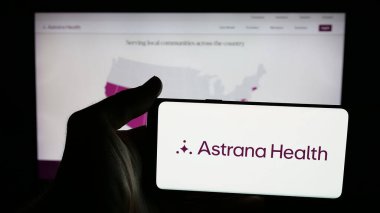Stuttgart, Germany - 11-12-2025: Person holding mobile phone with logo of US healthcare company Astrana Health Inc. on screen in front of web page. Focus on phone display.