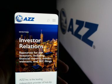 Stuttgart, Germany - 11-12-2025: Person holding smartphone with web page of US coating services company AZZ Inc. on screen in front of logo. Focus on center of phone display.