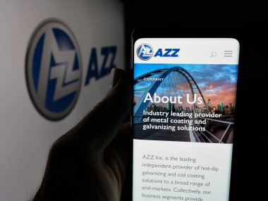 Stuttgart, Germany - 11-12-2025: Person holding cellphone with webpage of US coating services company AZZ Inc. on screen in front of logo. Focus on center of phone display.