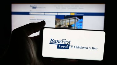 Stuttgart, Germany - 11-12-2025: Person holding mobile phone with logo of US financial company BancFirst Corporation on screen in front of web page. Focus on phone display.