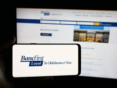 Stuttgart, Germany - 11-12-2025: Person holding smartphone with logo of US financial company BancFirst Corporation on screen in front of website. Focus on phone display.