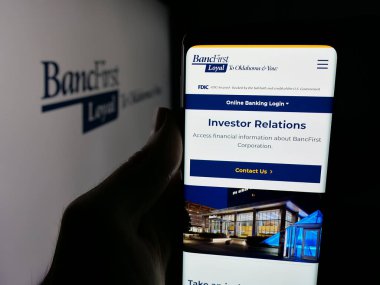 Stuttgart, Germany - 11-12-2025: Person holding smartphone with web page of US financial company BancFirst Corporation on screen in front of logo. Focus on center of phone display.