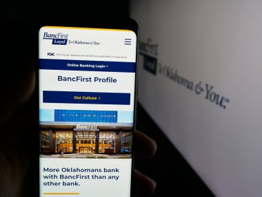 Stuttgart, Germany - 11-12-2025: Person holding cellphone with webpage of US financial company BancFirst Corporation on screen in front of logo. Focus on center of phone display.
