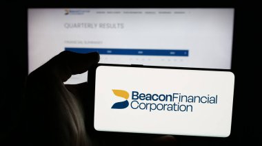 Stuttgart, Germany - 11-12-2025: Person holding mobile phone with logo of US banking company Beacon Financial Corp. on screen in front of web page. Focus on phone display.