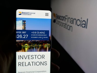 Stuttgart, Germany - 11-12-2025: Person holding cellphone with webpage of US banking company Beacon Financial Corp. on screen in front of logo. Focus on center of phone display.