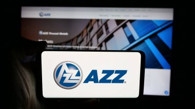Stuttgart, Germany - 11-12-2025: Person holding cellphone with logo of US coating services company AZZ Inc. on screen in front of webpage. Focus on phone display.