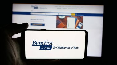 Stuttgart, Germany - 11-12-2025: Person holding cellphone with logo of US financial company BancFirst Corporation on screen in front of webpage. Focus on phone display.