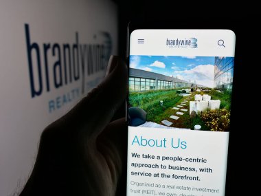 Stuttgart, Almanya - 11-13-2025: Emlak şirketi Brandywine Emlak Tröstü 'nün web sayfası logonun önünde duran kişi. Telefon ekranının merkezine odaklan.