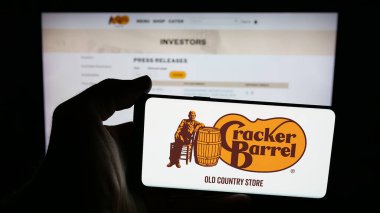 Stuttgart, Almanya - 11-14-2025: Üzerinde Cracker Barrel Old Country Store Inc. şirketinin logosu olan cep telefonu sahibi kişi web sayfasının önünde ekranda. Telefon ekranına odaklan.