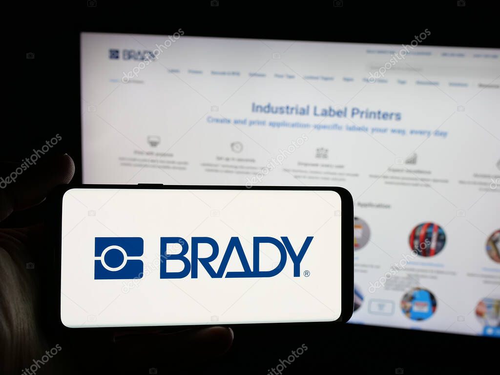 Stuttgart, Germany - 11-13-2025: Person holding smartphone with logo of US manufacturing company Brady Corporation on screen in front of website. Focus on phone display.