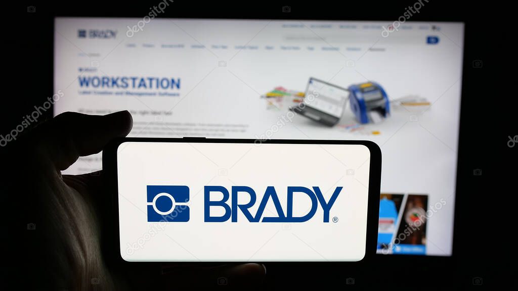 Stuttgart, Germany - 11-13-2025: Person holding cellphone with logo of US manufacturing company Brady Corporation on screen in front of webpage. Focus on phone display.