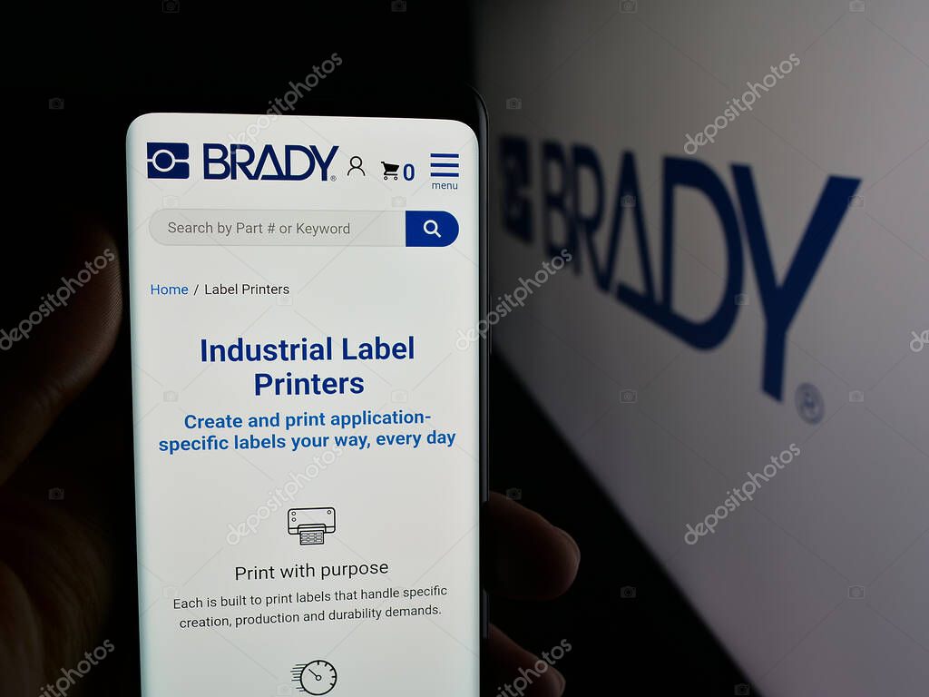 Stuttgart, Germany - 11-13-2025: Person holding cellphone with webpage of US manufacturing company Brady Corporation on screen in front of logo. Focus on center of phone display.