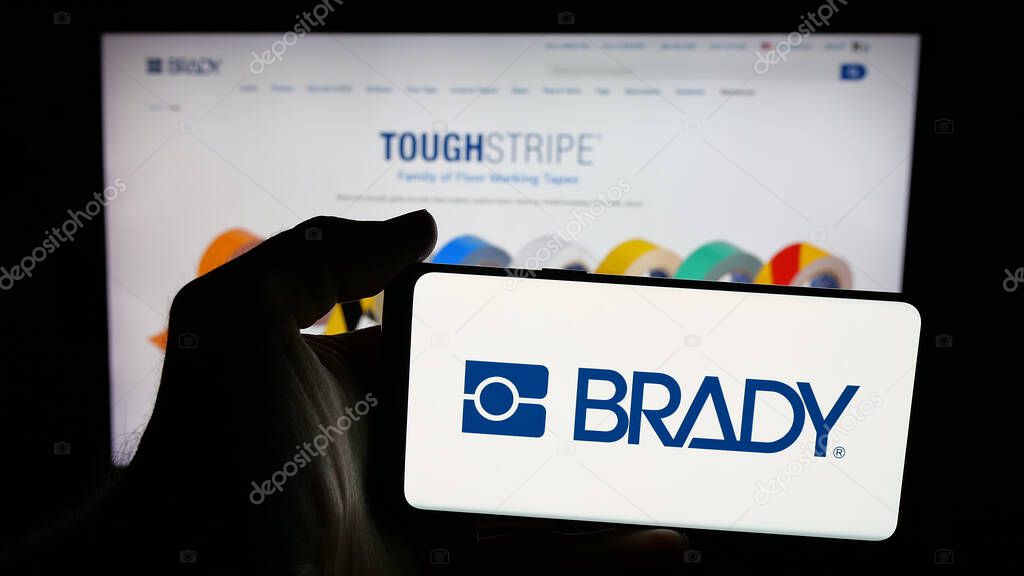 Stuttgart, Germany - 11-13-2025: Person holding mobile phone with logo of US manufacturing company Brady Corporation on screen in front of web page. Focus on phone display.