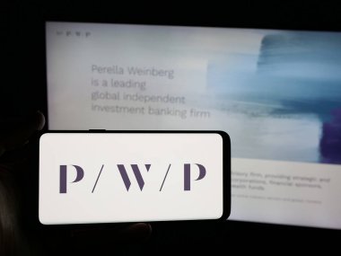 Stuttgart, Almanya - 11-19-2025: Web sitesi önünde ekranda ABD 'li Perella Weinberg Partners (PWP) şirketinin logosunun bulunduğu akıllı telefon sahibi kişi. Telefon ekranına odaklan.