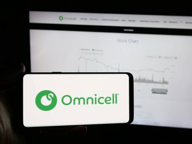 Stuttgart, Almanya - 11-20-2025: Sağlık hizmetleri teknoloji şirketi Omnicell Inc. 'in logosuna sahip akıllı telefonu web sitesinin önünde tutan kişi. Telefon ekranına odaklan.