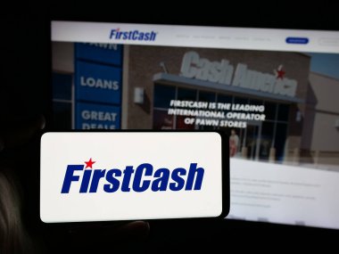 Stuttgart, Almanya - 11-20-2025: ABD 'li rehinci firması FirstCash Holding Inc.' in logosunu elinde tutan kişi web sitesinin önünde ekranda. Telefon ekranına odaklan.