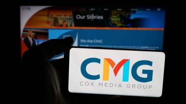 Stuttgart, Almanya - 11-23-2025: Web sayfası önünde ekranda ABD 'li CMG Media Corporation (Cox Media) logosu olan cep telefonu sahibi kişi. Telefon ekranına odaklan.