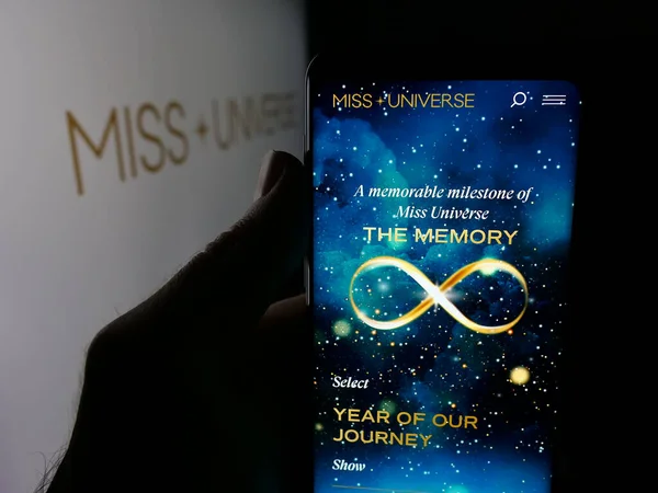 Stuttgart, Almanya - 11-23-2025: Güzellik yarışması organizasyonu web sitesi Miss Universe 'in akıllı telefonunu logonun önünde tutan kişi. Telefon ekranının merkezine odaklan.