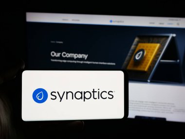 Stuttgart, Almanya - 11-24-2025: İnternet sitesinin önünde ekranda ABD 'li nöral ağ şirketi Synaptics Inc.' in logosuna sahip akıllı telefonu tutan kişi. Telefon ekranına odaklan.