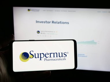 Stuttgart, Almanya - 11-26-2025: ABD 'li Supernus Pharmaceuticals Inc. şirketinin logosunu elinde tutan kişi web sitesinin önünde ekranda. Telefon ekranına odaklan.
