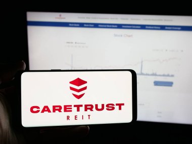 Stuttgart, Almanya - 11-27-2025: ABD 'li emlak şirketi CareTrust REIT Inc.' in logosunu elinde tutan kişi web sitesinin önünde ekranda. Telefon ekranına odaklan.
